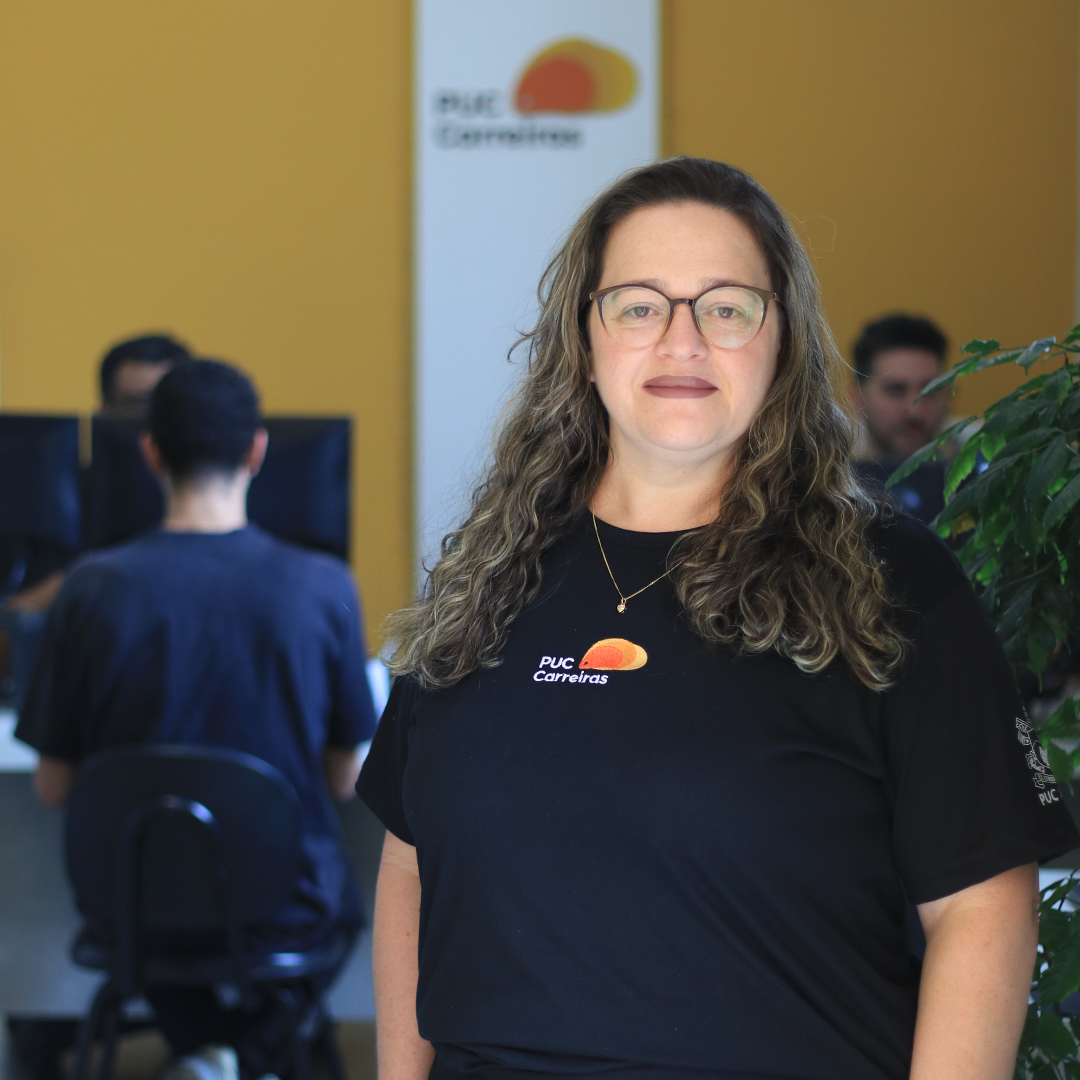 Foto de mulher com cabelos longos cacheados e com roupa preta e marca da PUC Carreiras na porta do setor