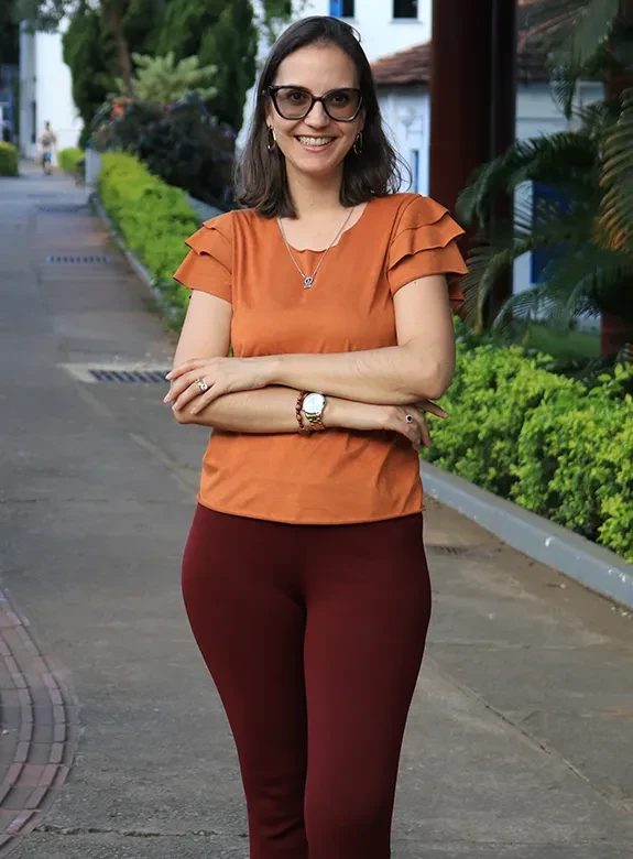 Jovem egressa de cabelos escuros e roupa laranja, no Campus da PUC Minas Coração Eucarístico