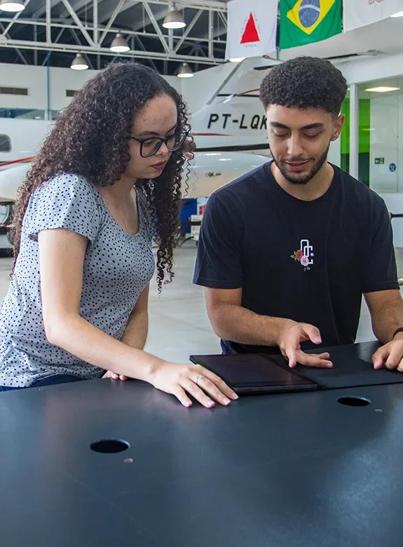 Mulher e homem jovens sentados em bancada de laboratório de Aeronáutica