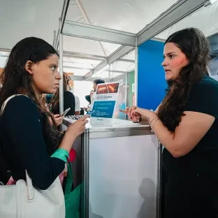 Visitante conversa com expositora da Feira de Carreiras PUC Minas 2025