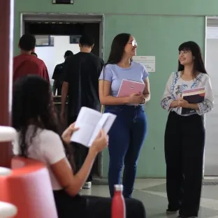 Alunas com livros nas mãos andando em ambiente da Universidade