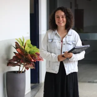 Mulher jovem de cabelos cacheados segurando notebook andando em corredor da Universidade