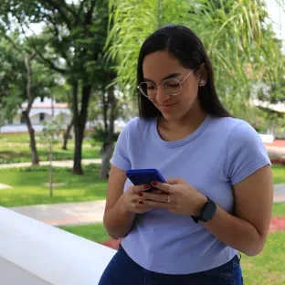 Aluna usando celular no jardim da PUC Minas